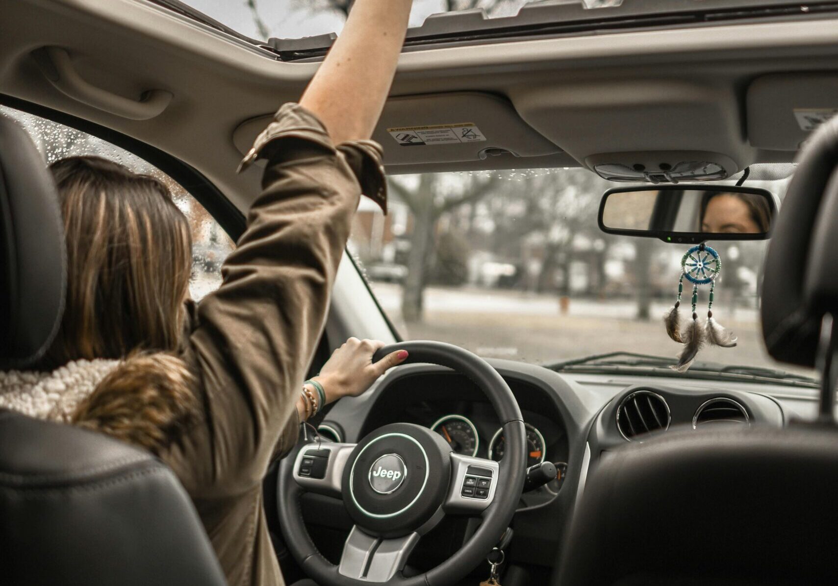 A young woman enjoying a drive with the sunroof open, showing car interior detail.