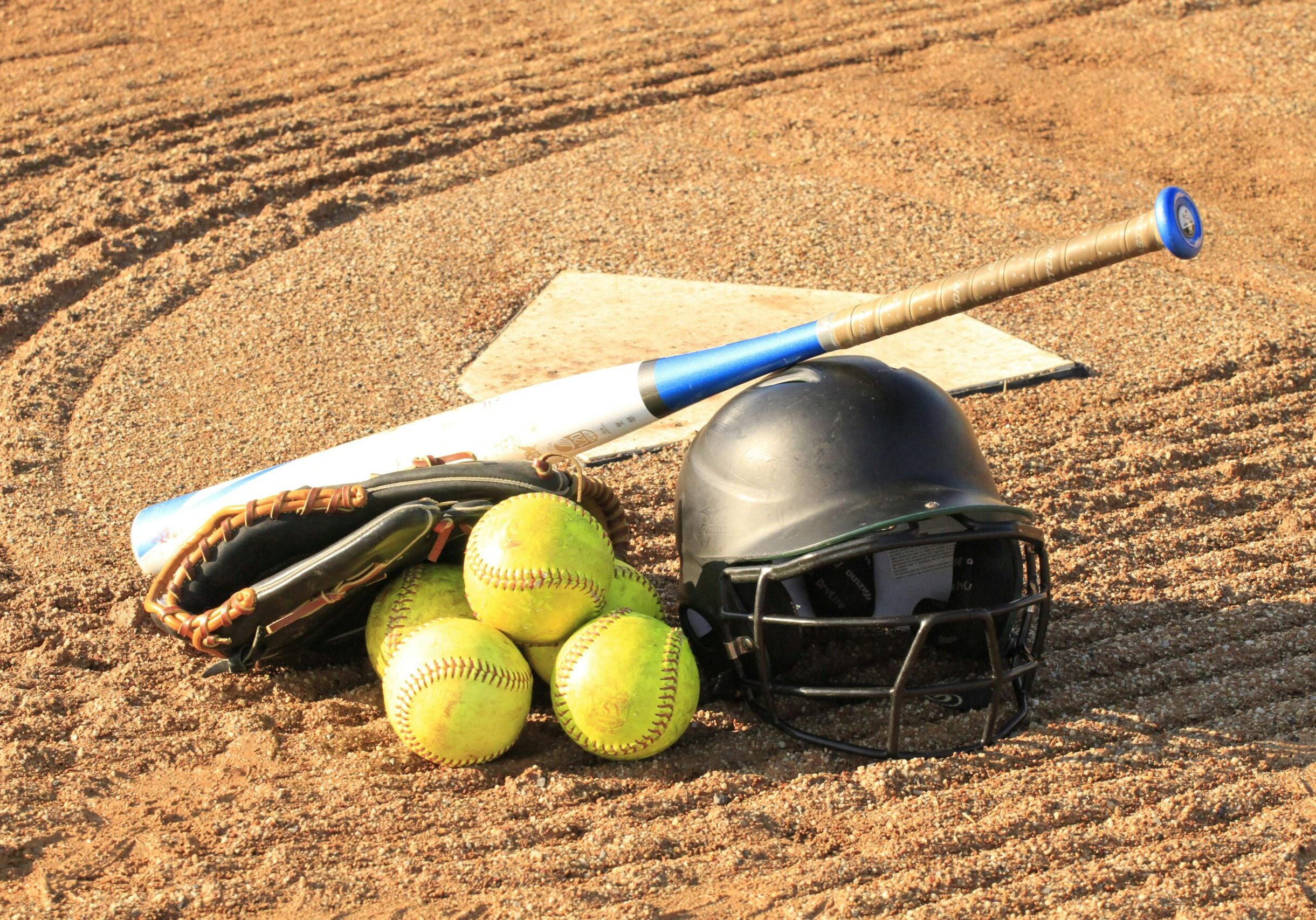 Close-up of baseball and softball gear on a dirt field, ready for a game.